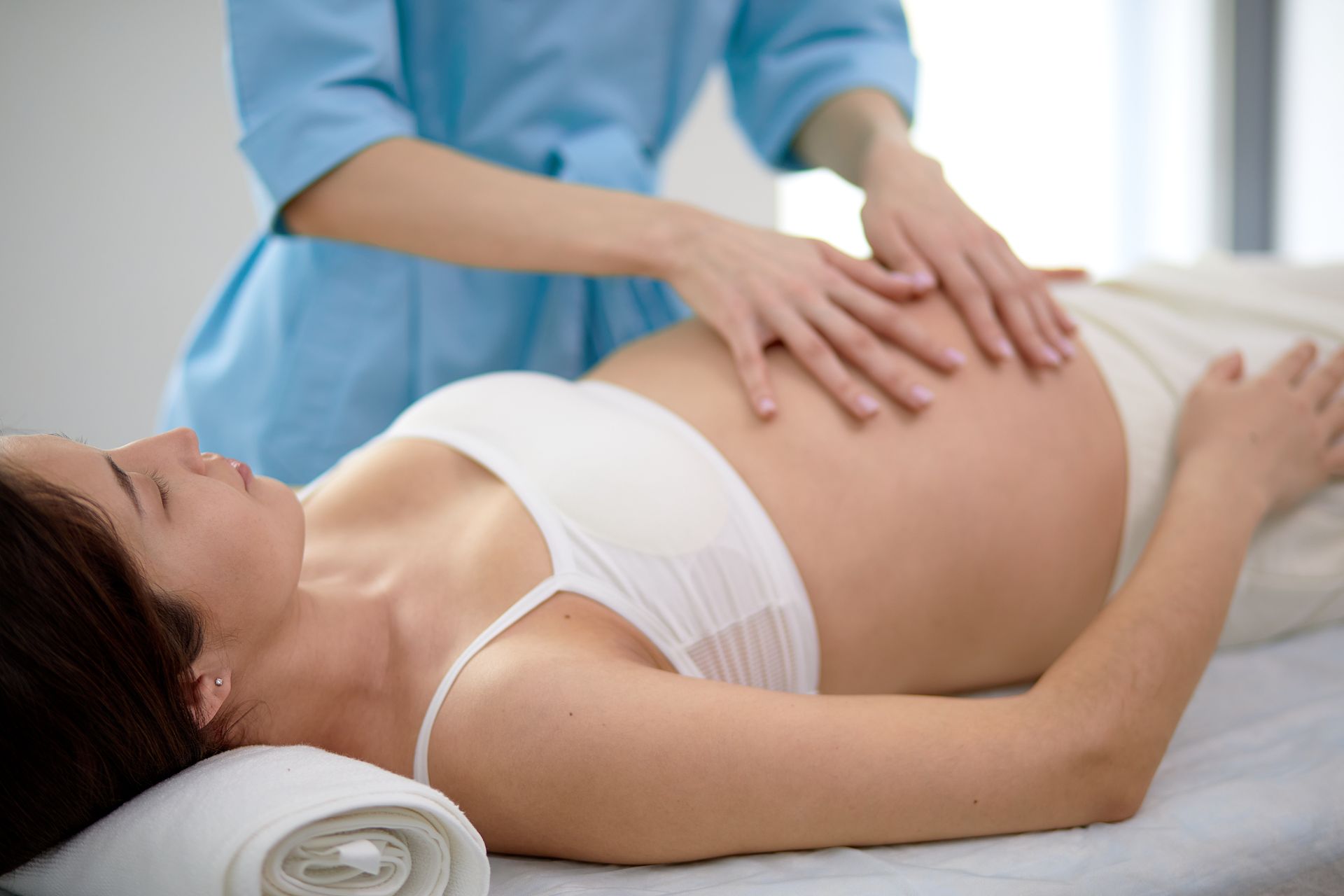 Pregnant person receiving massage on abdomen. Light skin, white top, blue scrub top.