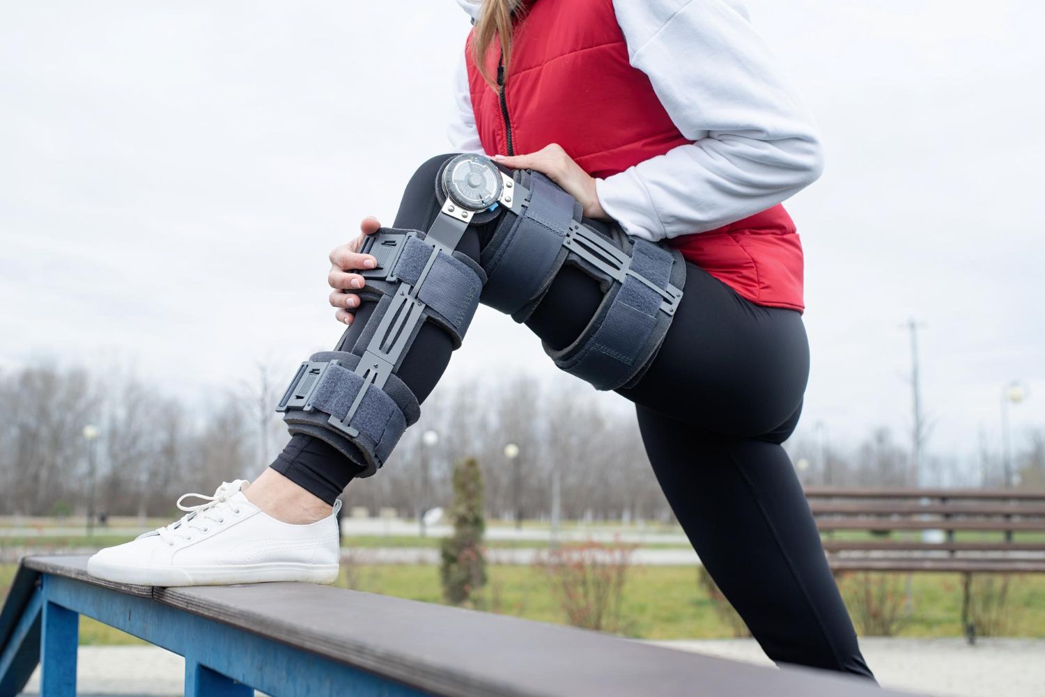 A woman wearing a knee brace is sitting on a bench.