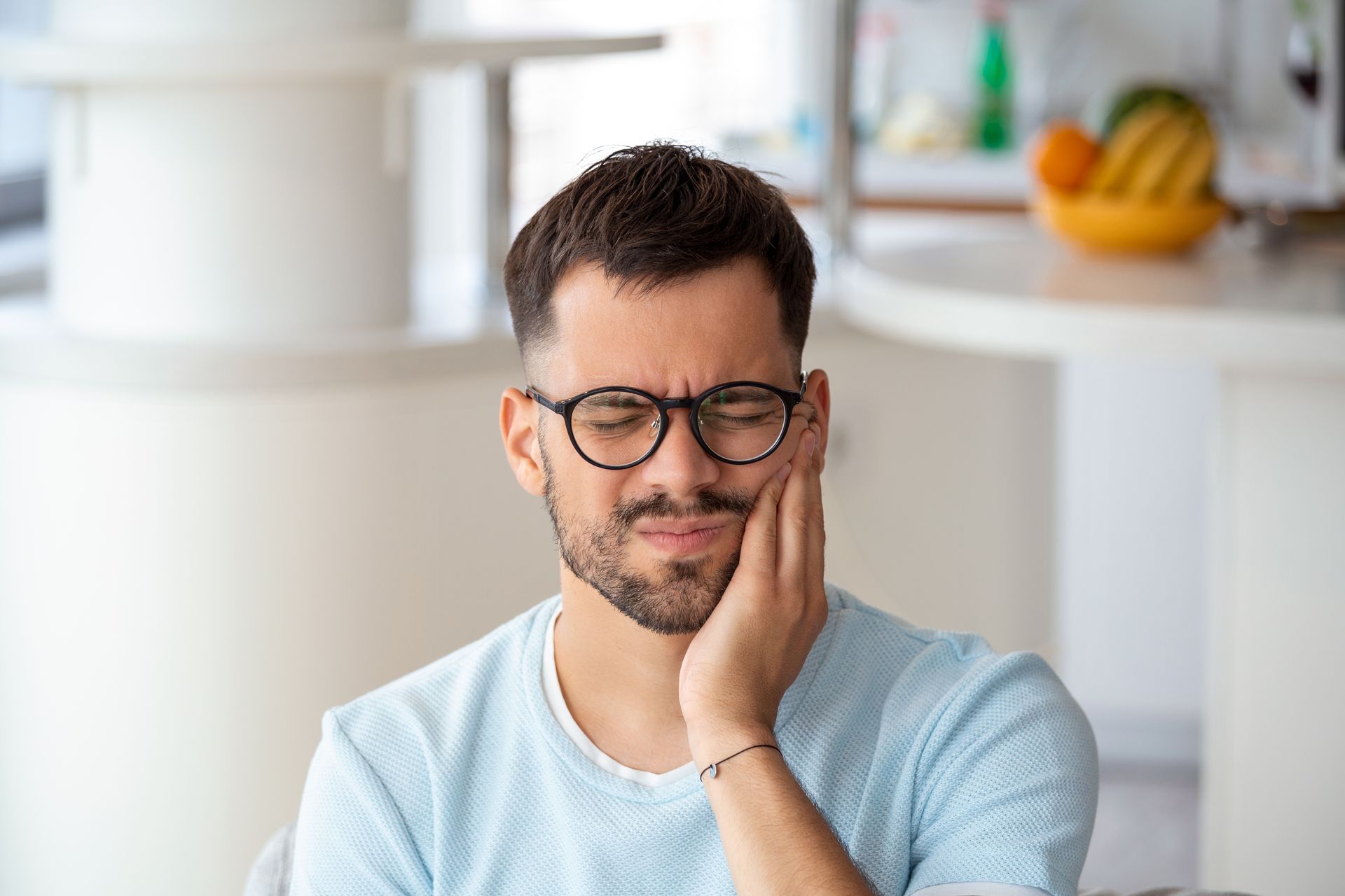 A man with glasses is holding his face in pain because of a toothache.