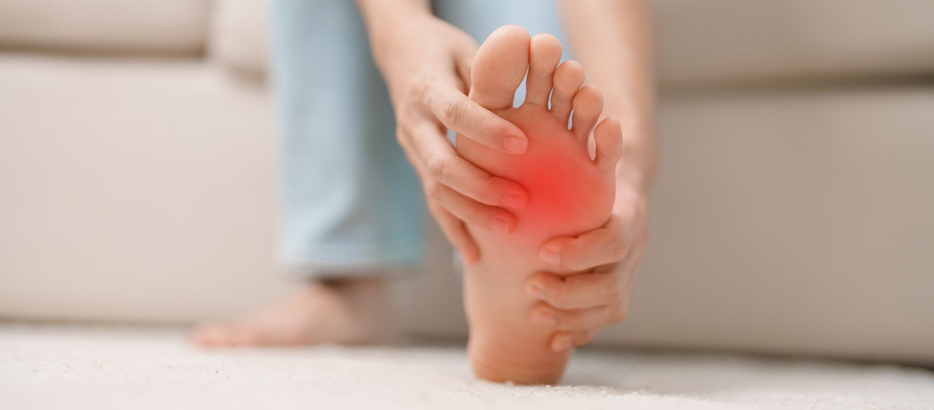 A woman is sitting on a couch holding her foot in pain.