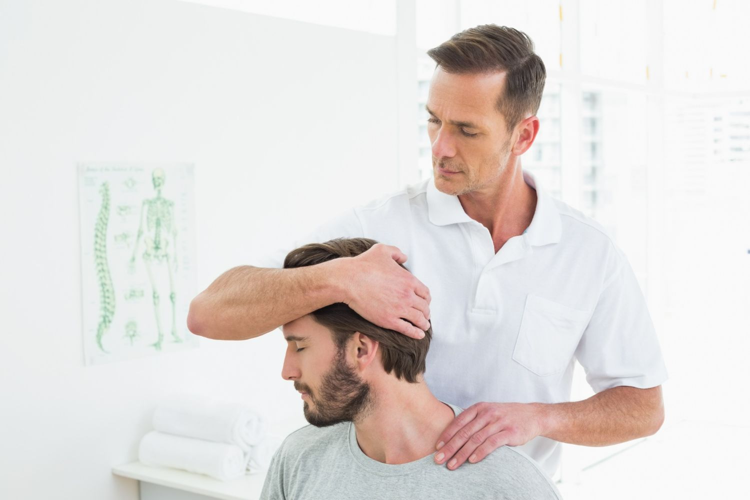 Physical therapist examining a man’s neck in a bright clinic room