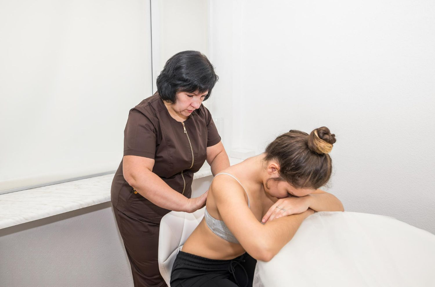 Massage therapist working on a woman’s back on a massage table in a bright room