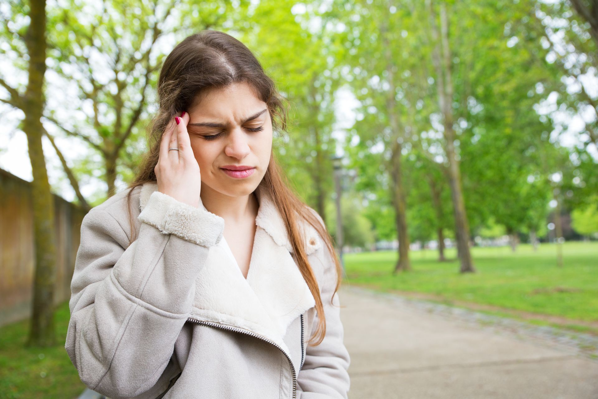 A woman is standing in a park with a headache.