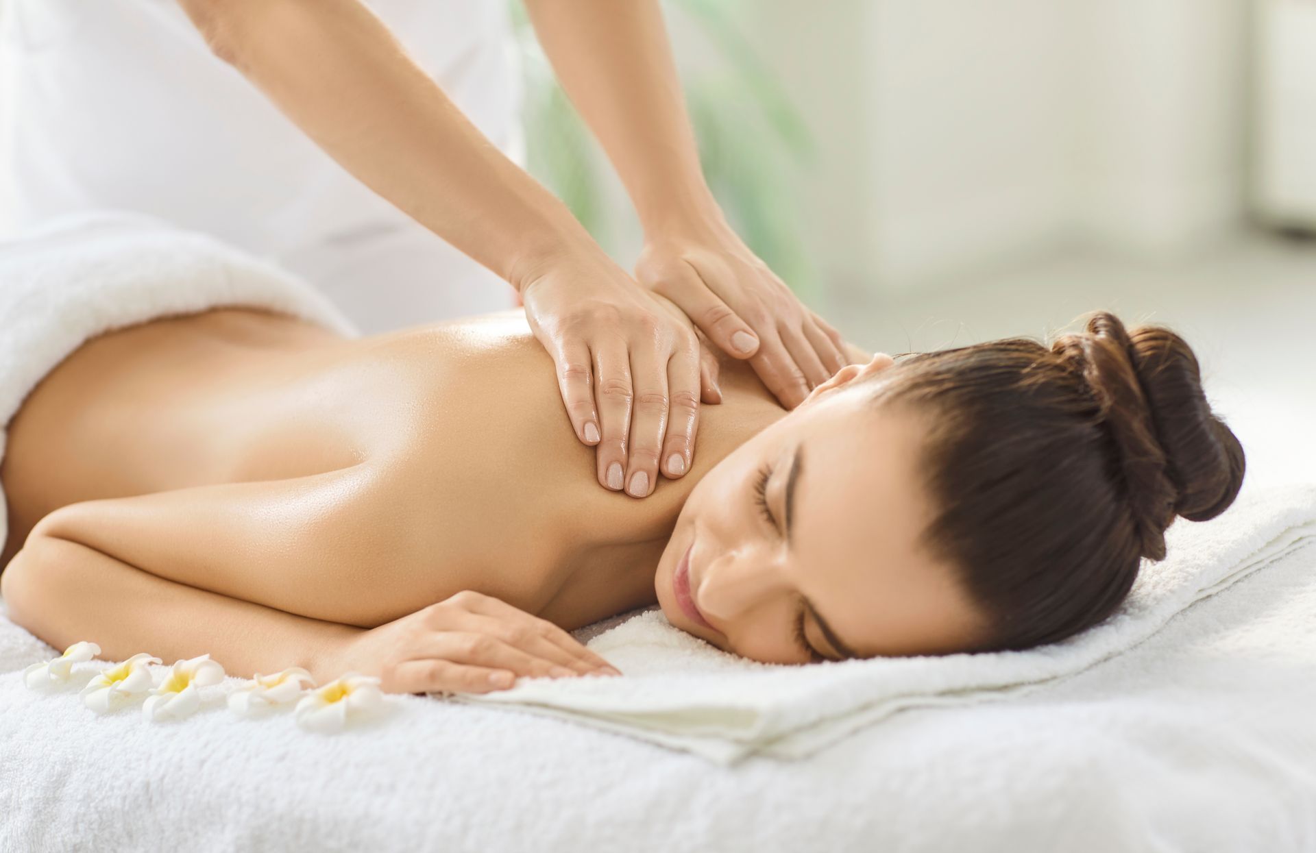 Woman receiving a back massage, lying face down on a white towel, in a spa setting.