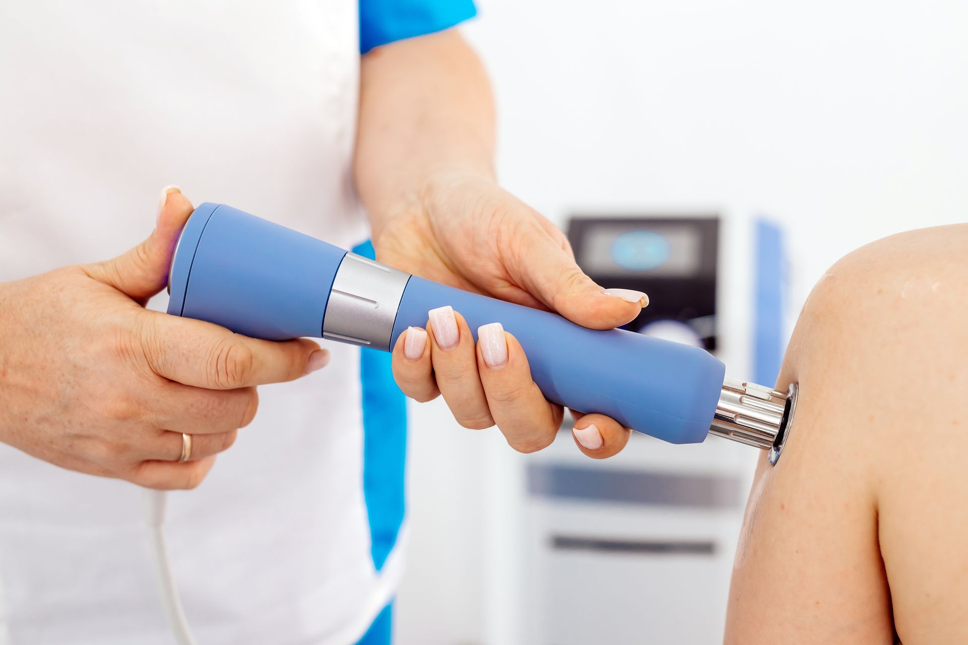 A person's knee being treated with a blue shockwave therapy device by a healthcare professional.