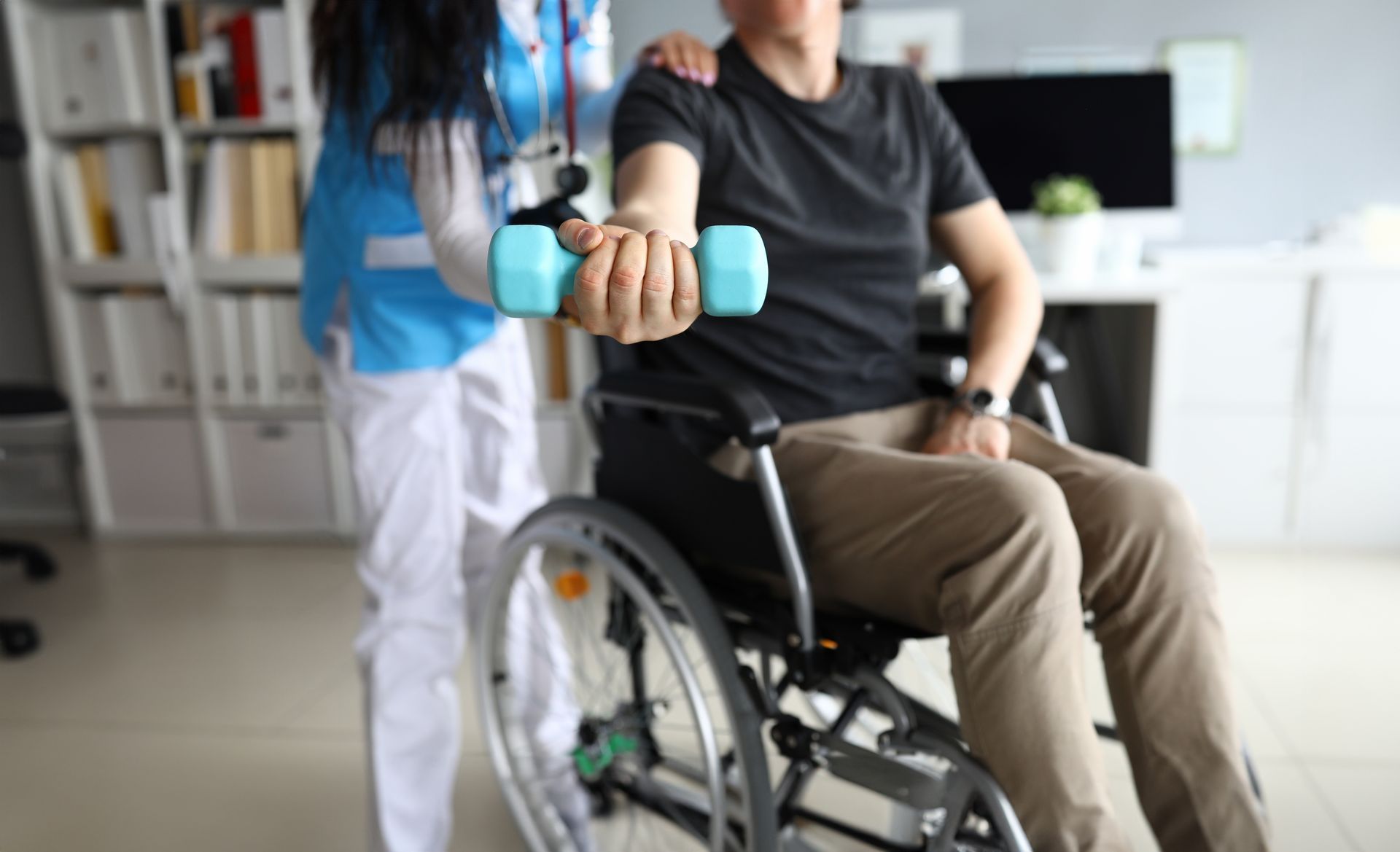 A nurse is helping a man in a wheelchair with a dumbbell.