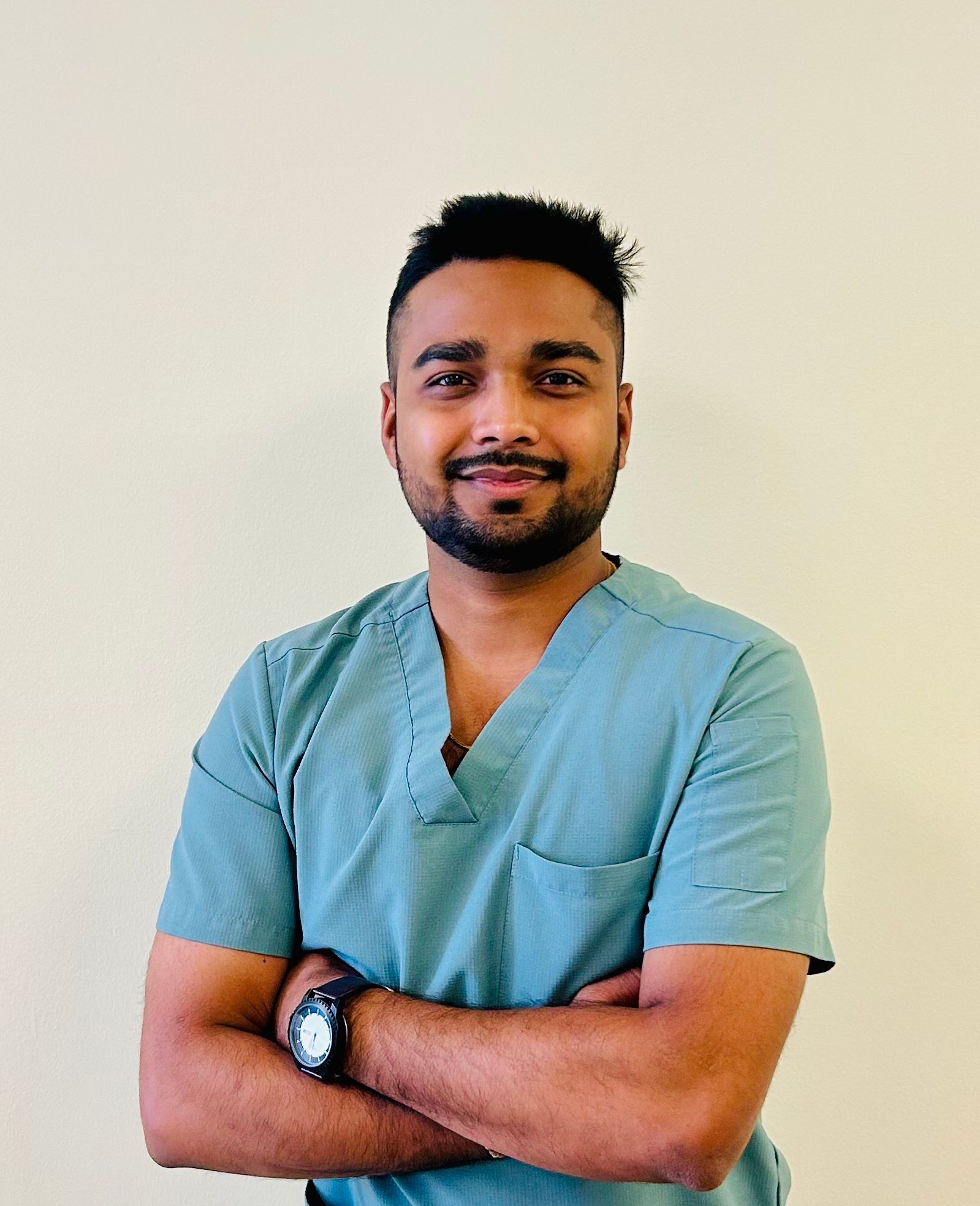 Man in teal scrubs smiling with arms crossed, wearing a watch.