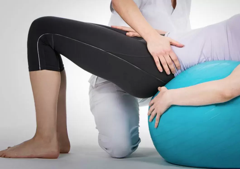 A woman is kneeling down next to a blue exercise ball