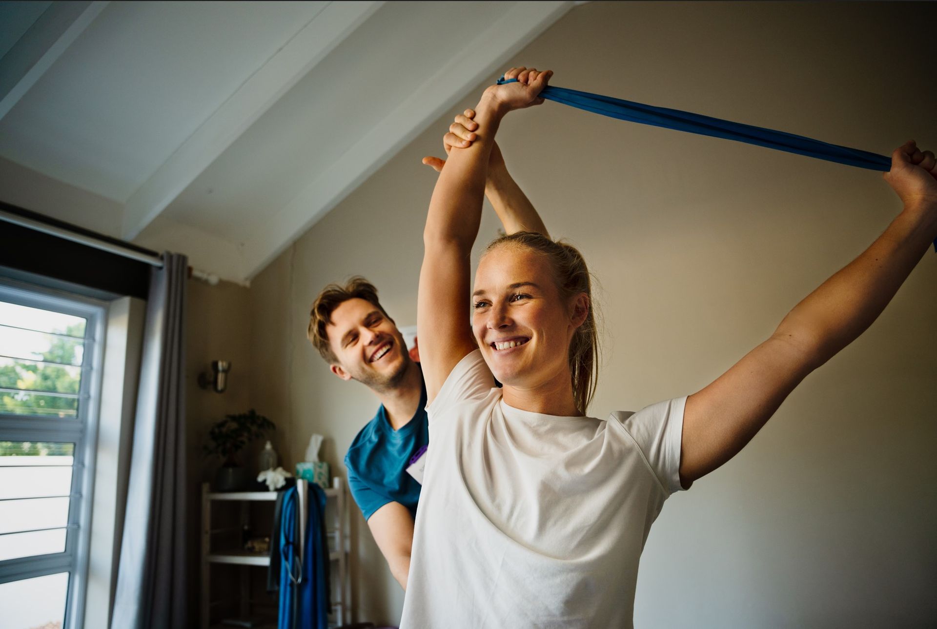 A man is helping a woman stretch her arms with a resistance band.