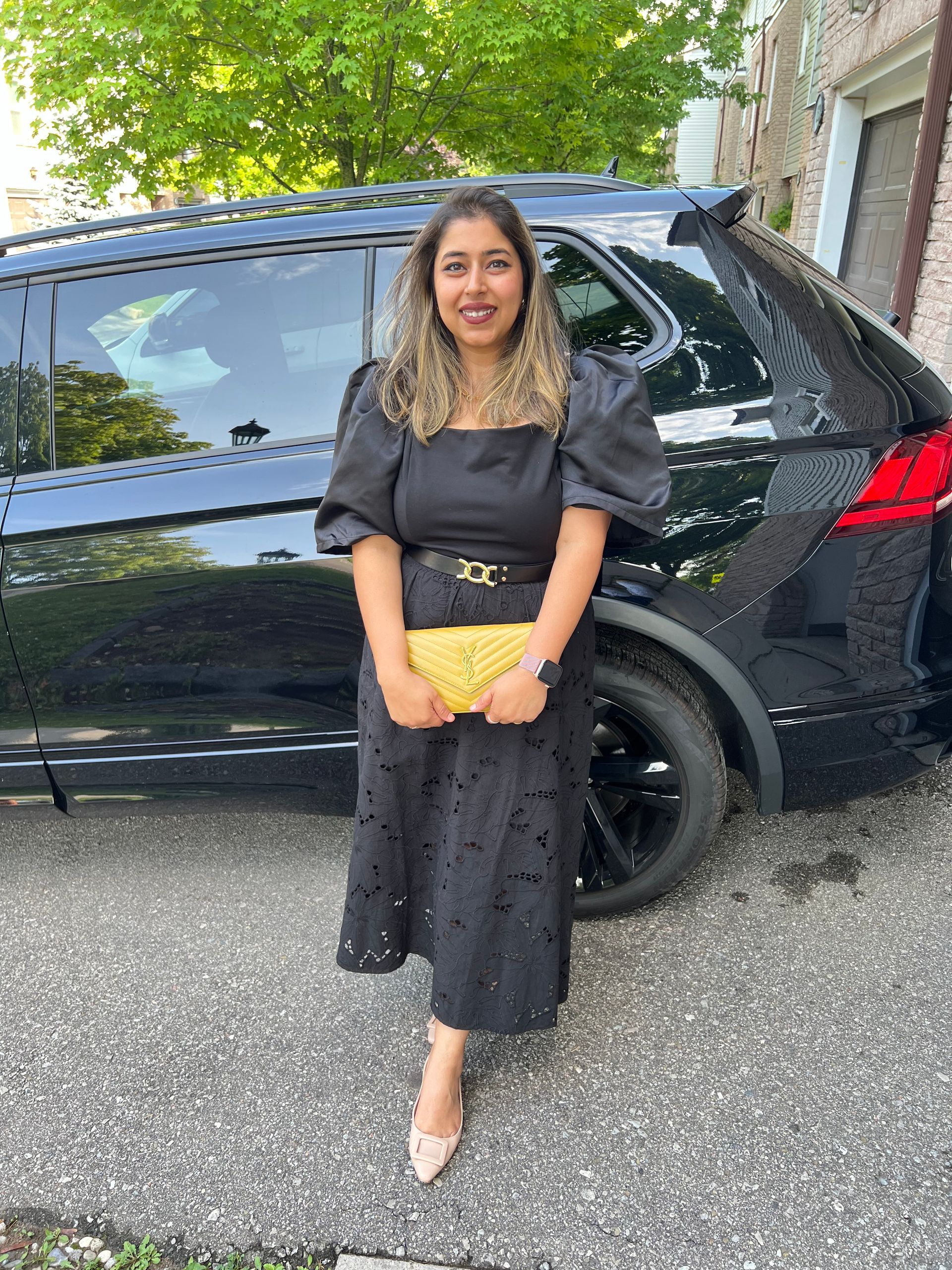 A woman in a black dress is standing in front of a black car.