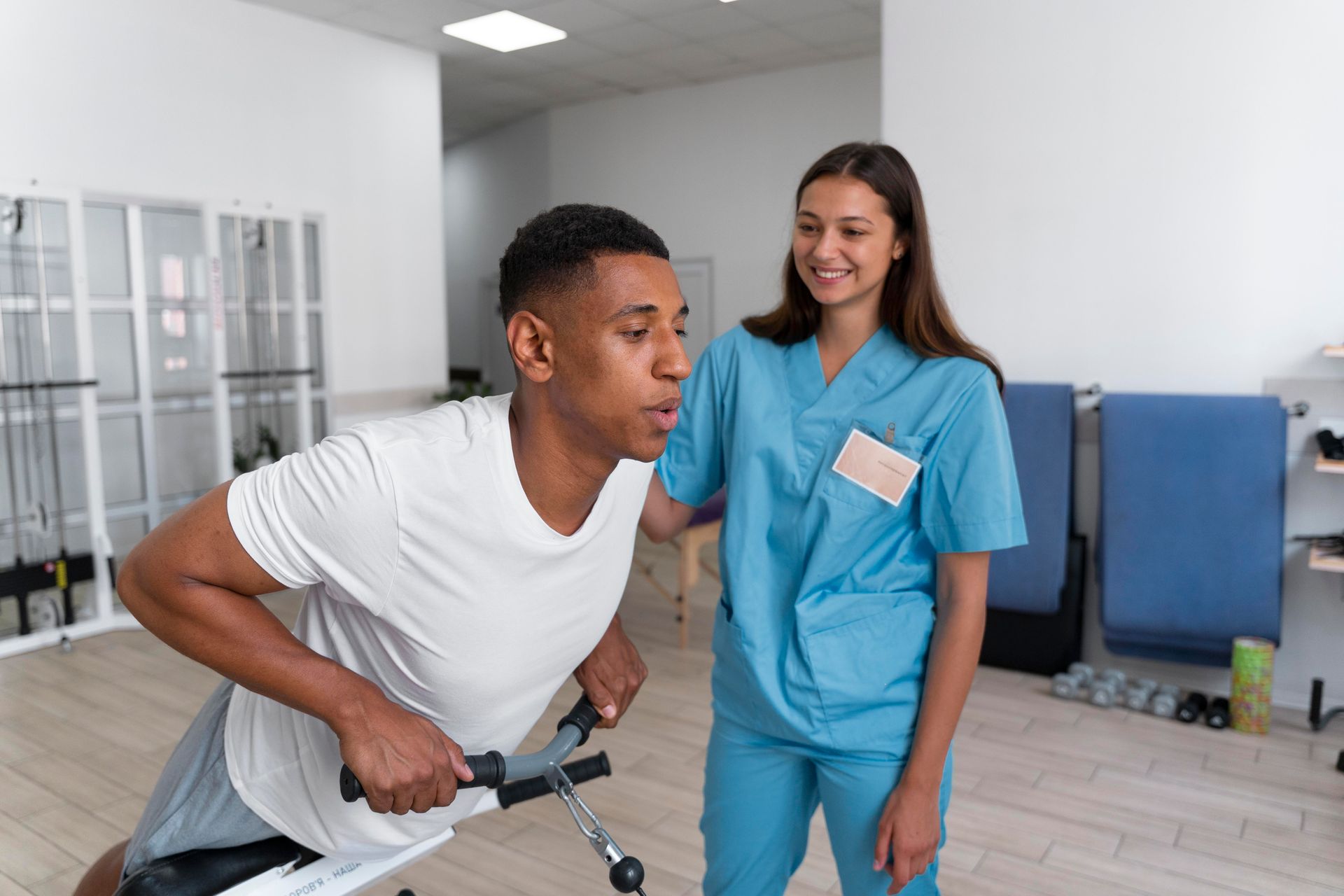 A man is doing exercises on a machine while a nurse watches.
