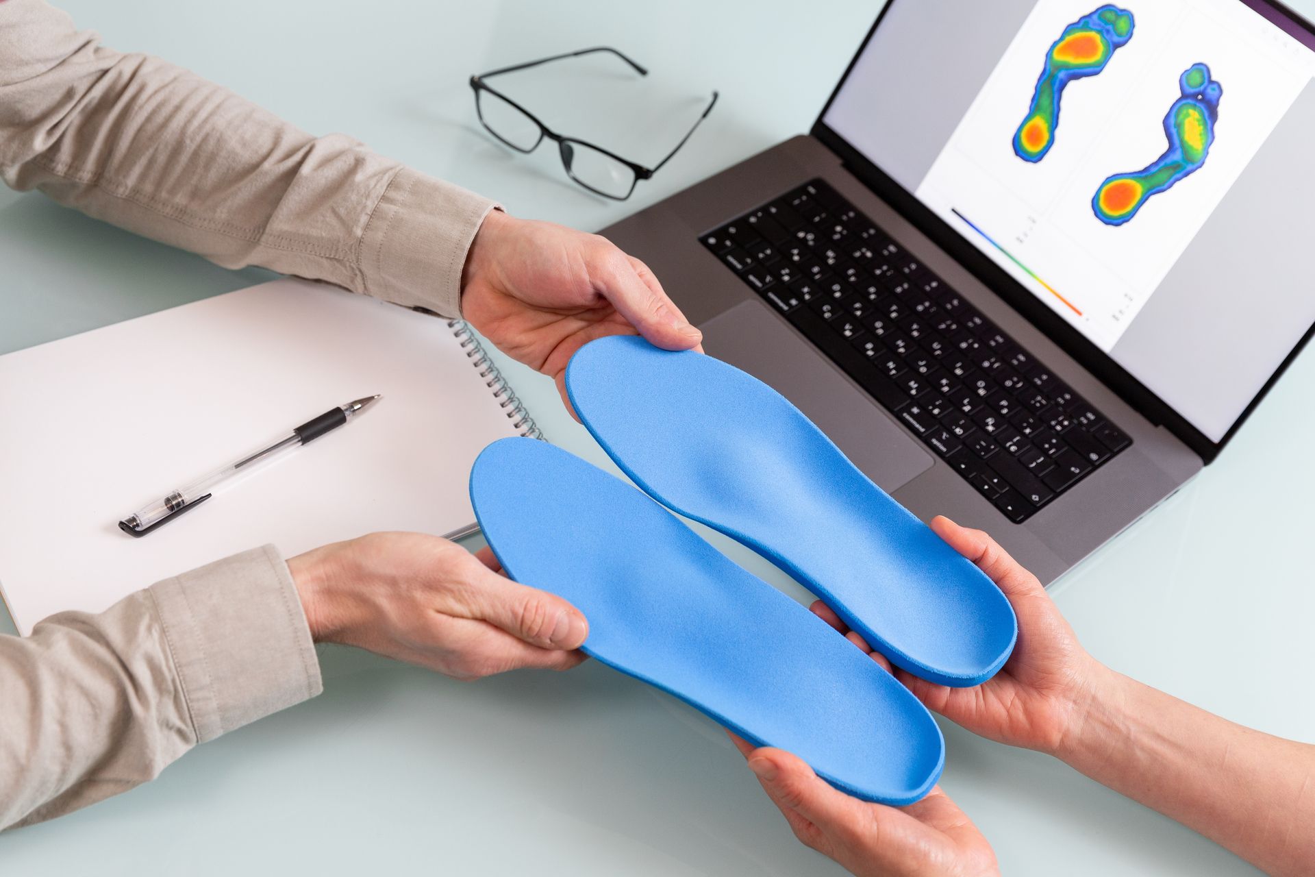 A person is holding a pair of blue insoles in front of a laptop computer.