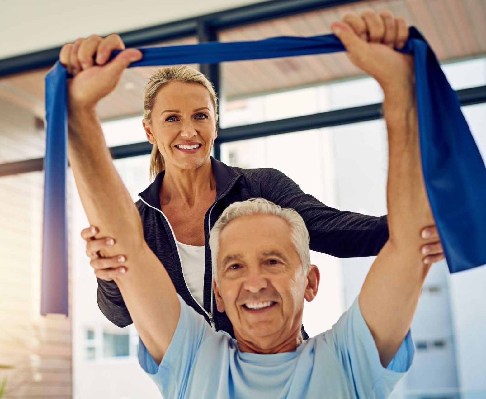 A woman is helping an older man with a resistance band.