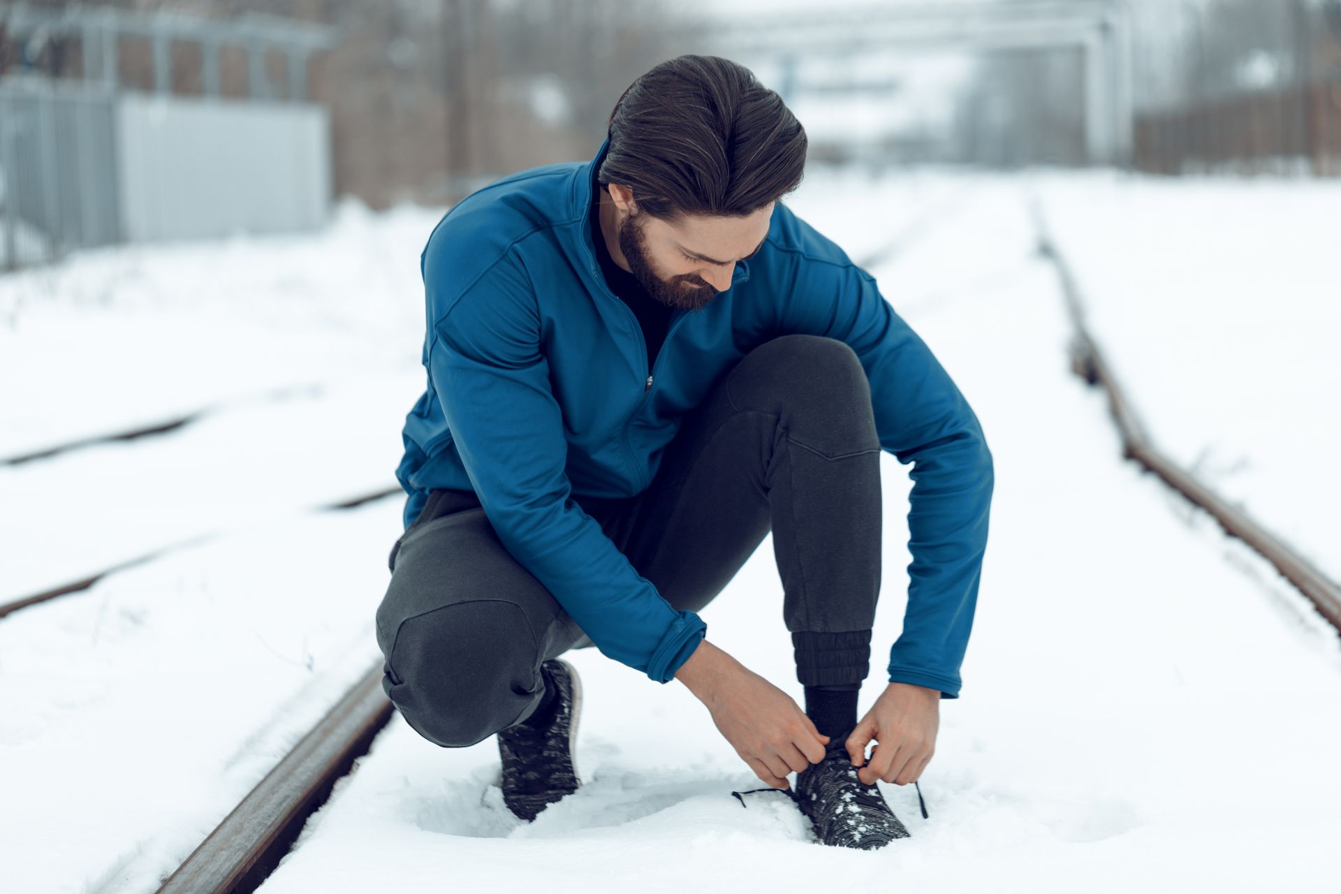 A man is kneeling down in the snow tying his shoes.