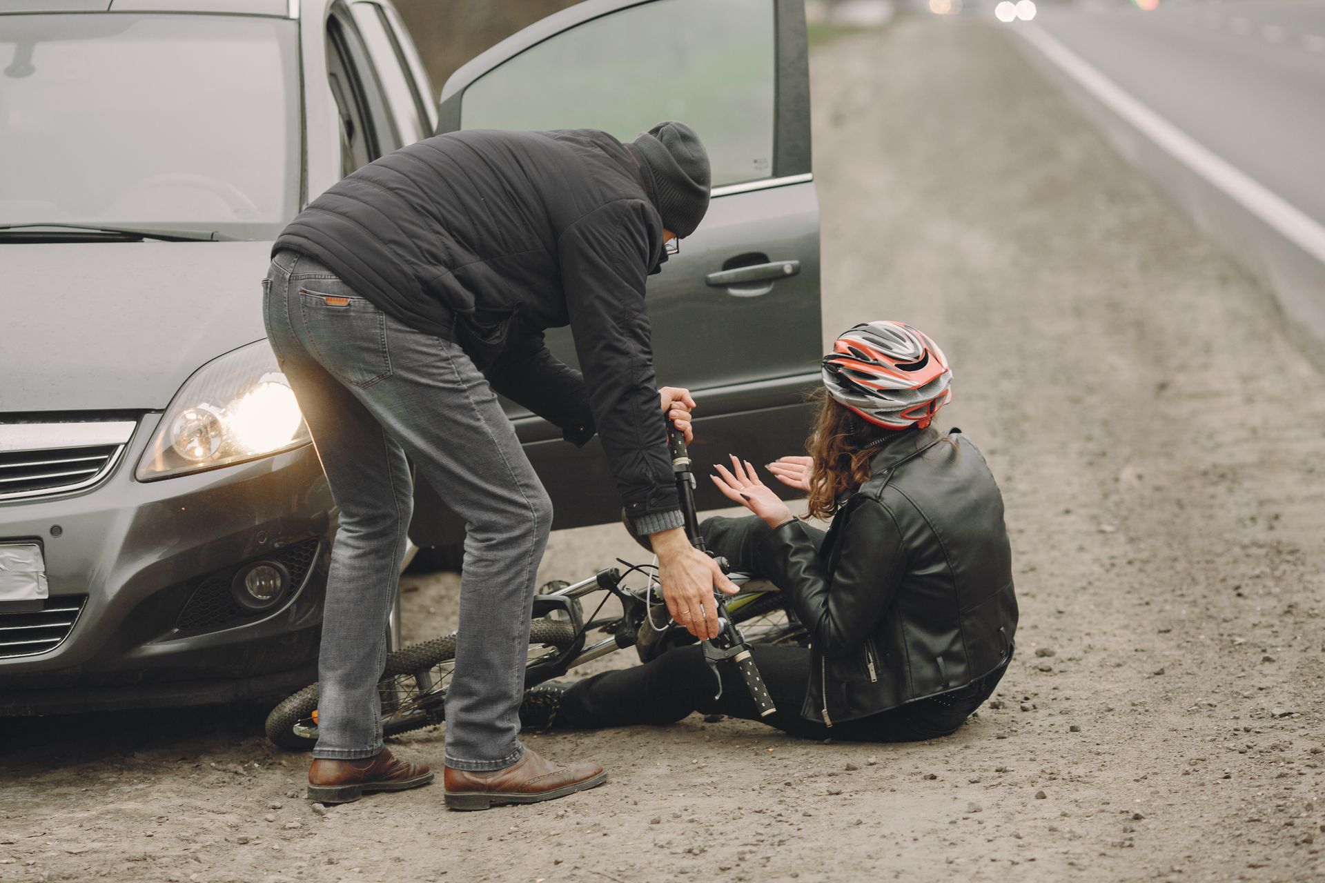 A man is helping a woman who is sitting on the ground next to a car.