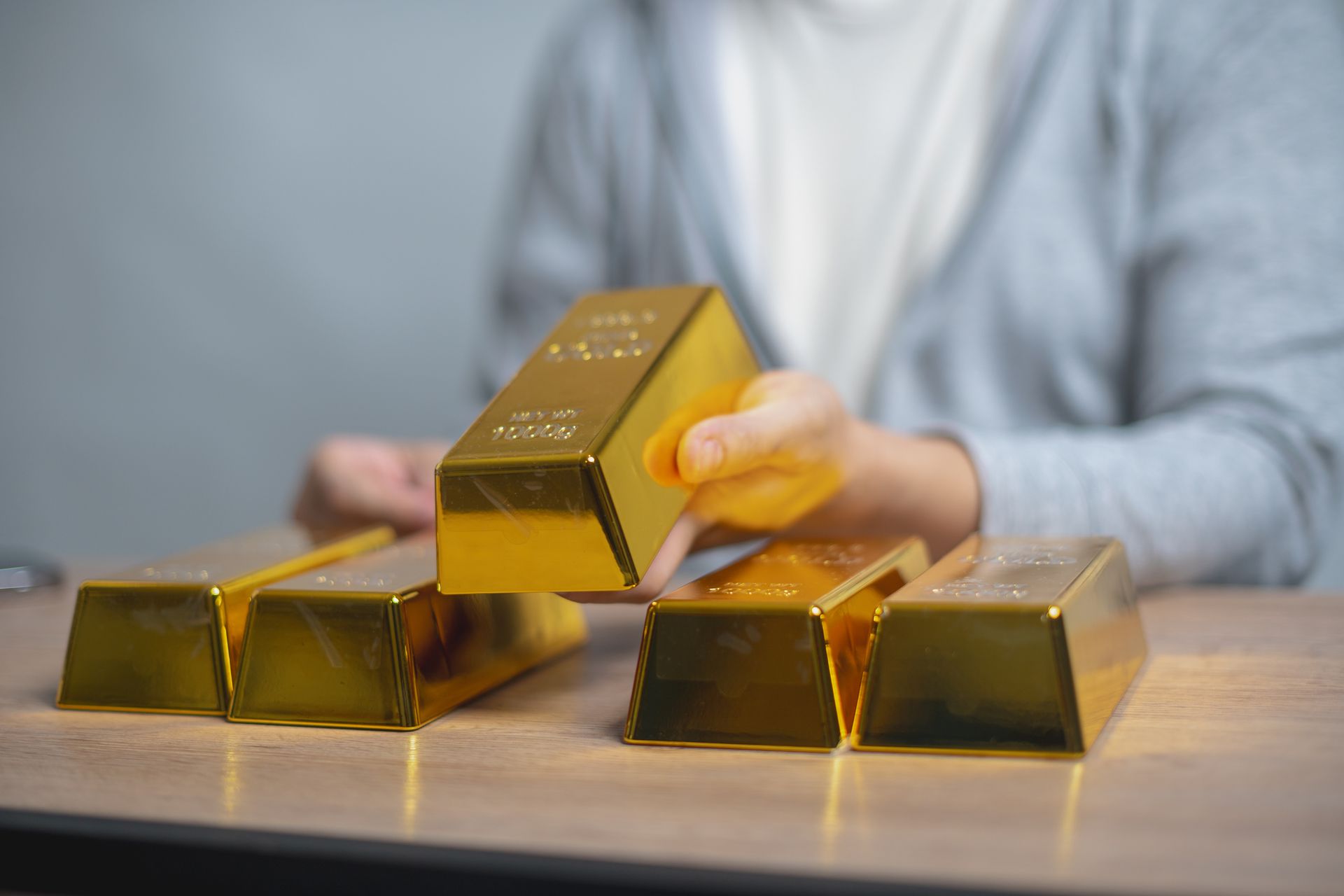 A person stacking gold bars on a table, representing investment in physical precious metals. A person stacking gold bars on a table, representing investment in physical precious metals.