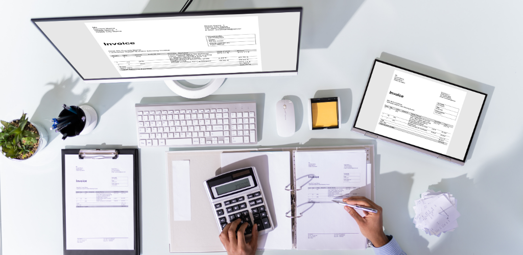 Overhead view of a person using a calculator and reviewing documents at a desk with a computer monitor.