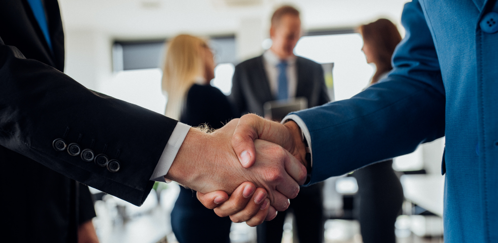 People in suits shake hands in an office, with smiling faces.