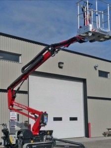 Une nacelle élévatrice rouge est garée devant un immeuble.