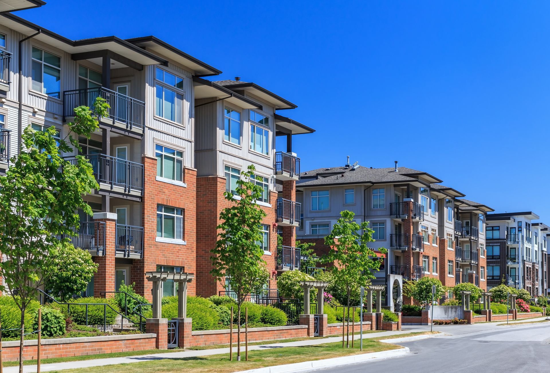 Multi-story brick and grey apartment buildings with balconies against a clear blue sky.
