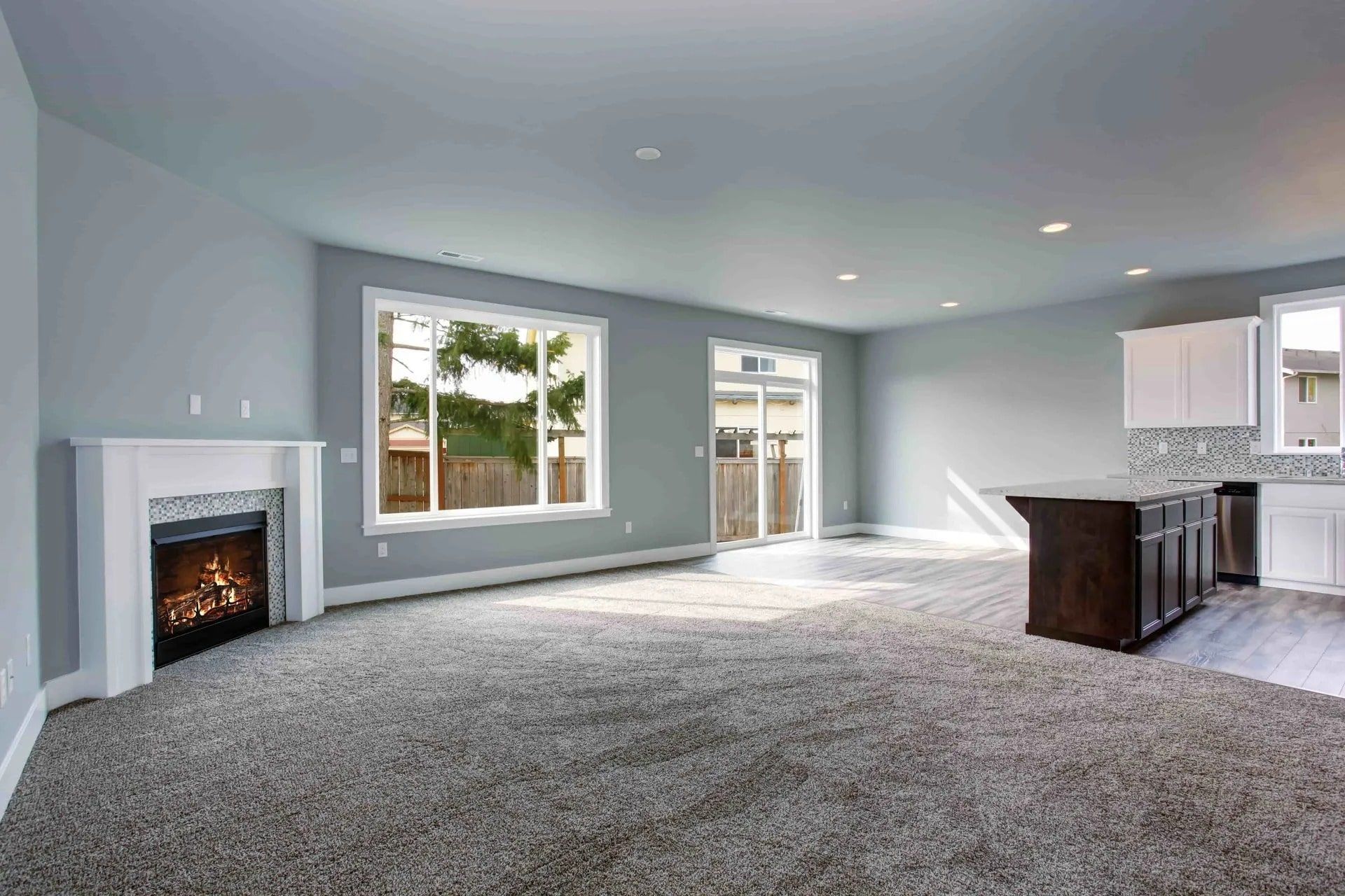 Empty living room with gray carpet, fireplace, and kitchen island.