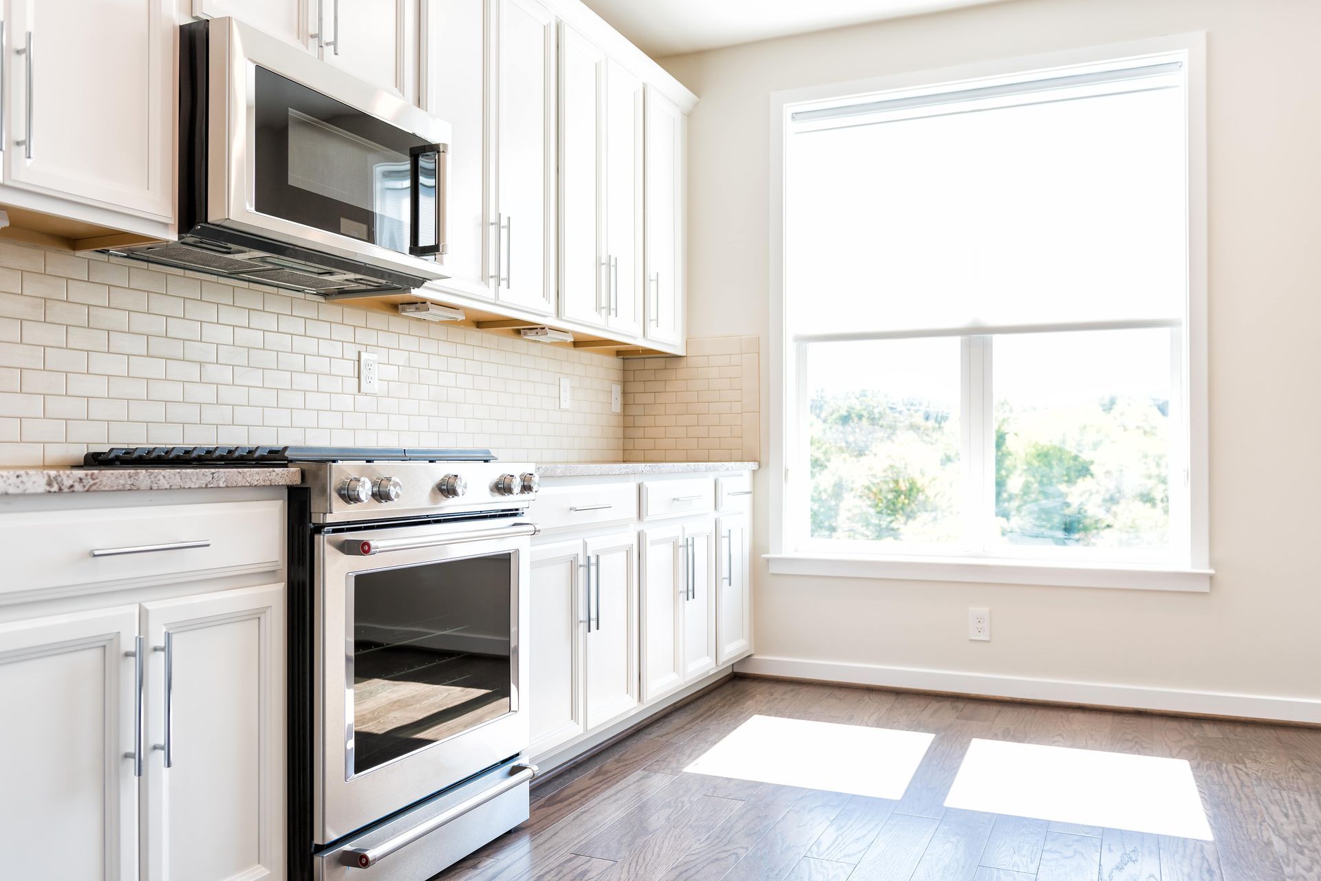 Bright, modern kitchen with white cabinets, stainless steel appliances, and a window providing natural light.