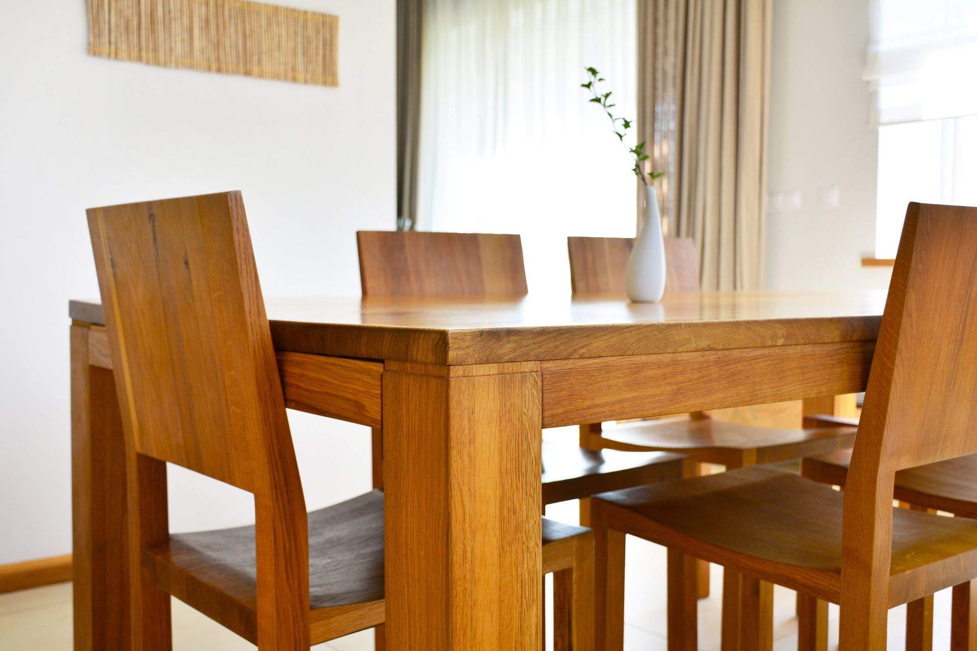 Wooden dining table and chairs in a bright room with a white wall and a small vase.
