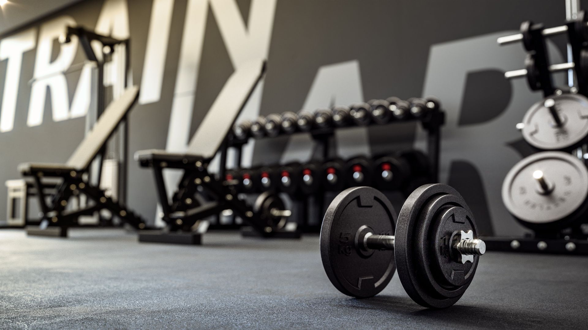 Dumbbell on gym floor with weight bench and rack of weights in background.