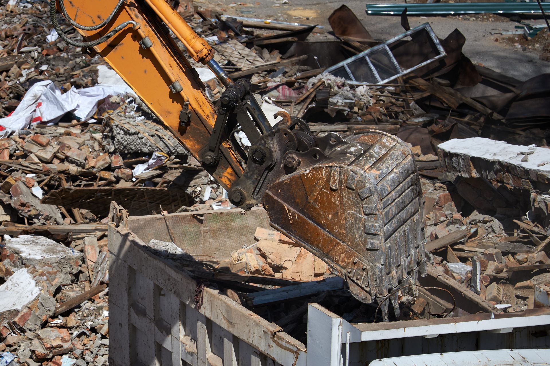 A yellow excavator bucket reaching into a pile of construction debris and rubble.