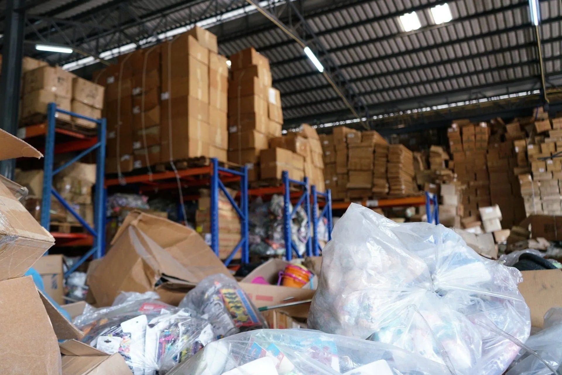 Warehouse interior with stacked cardboard boxes on blue shelving units and a pile of debris in the foreground.