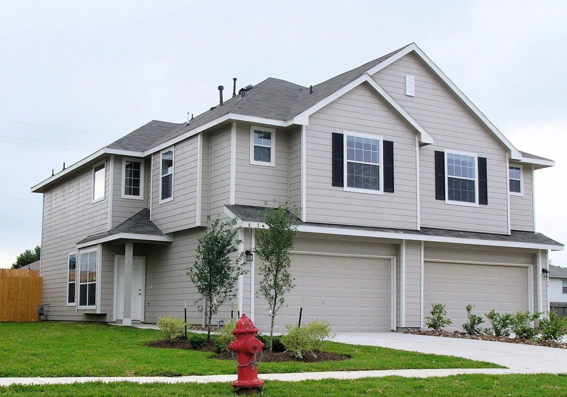 Two-story house with light siding and two garage doors; red fire hydrant in front yard.