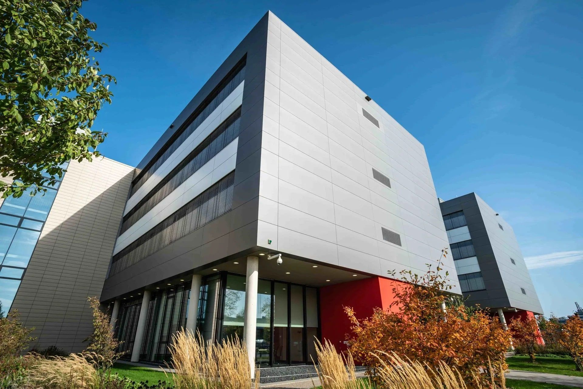 Modern gray and red building with large windows under a clear blue sky.