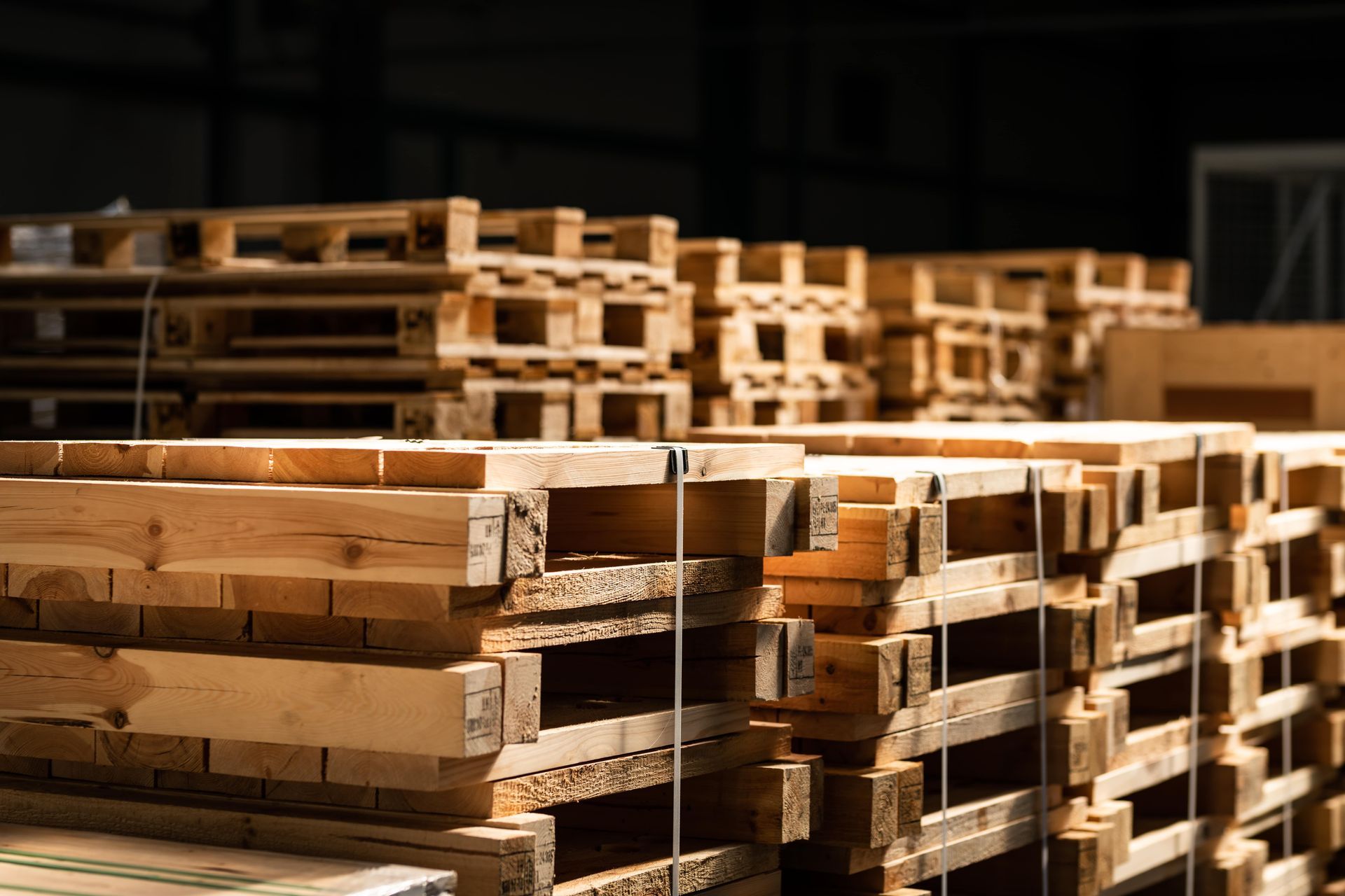 Wooden pallets stacked in a warehouse, some in foreground and others in background.