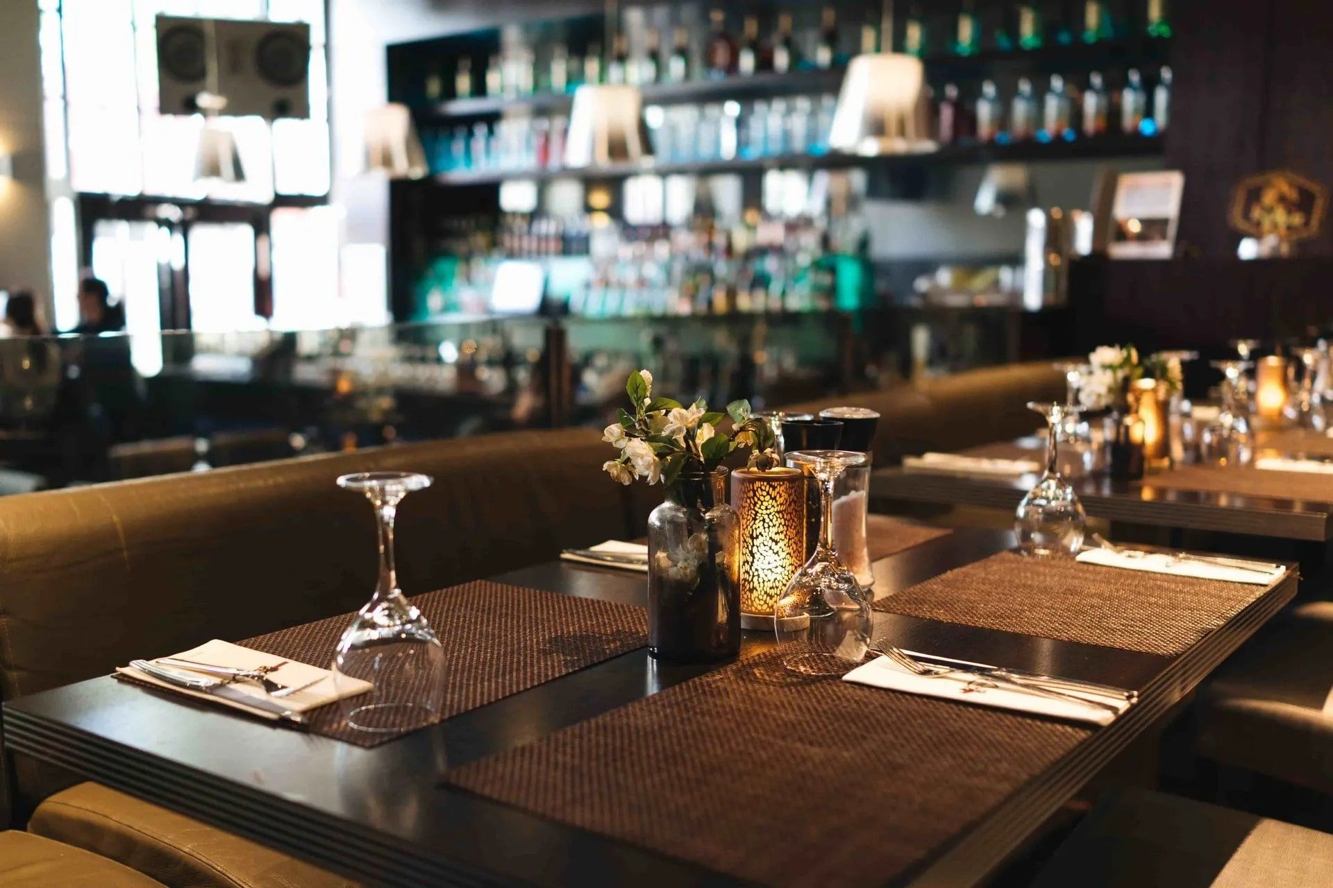Restaurant table setting with glassware, silverware, and centerpiece in front of a bar.