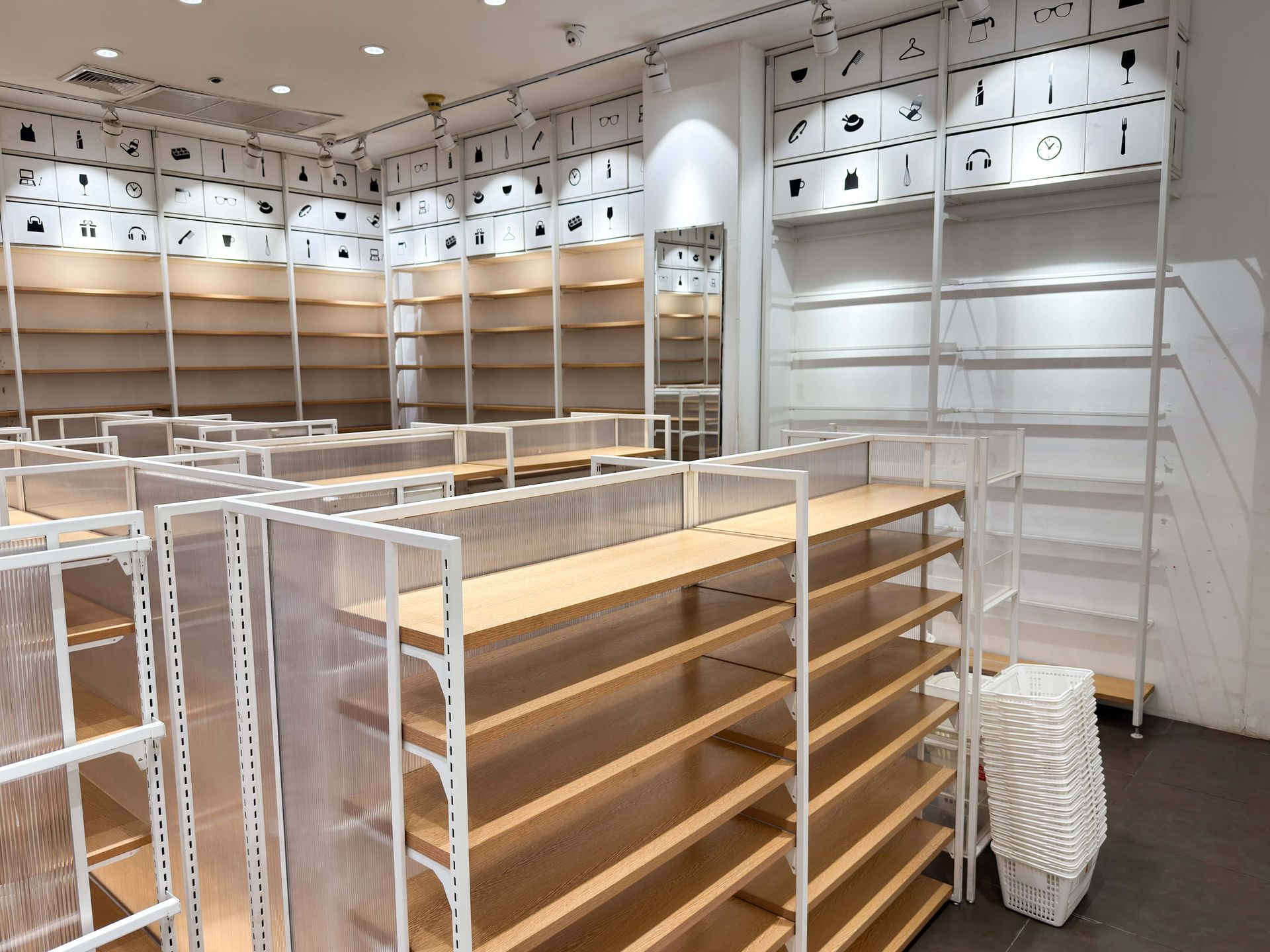 Empty store shelves; white metal frames with wooden shelves. A few cardboard boxes near shelves.