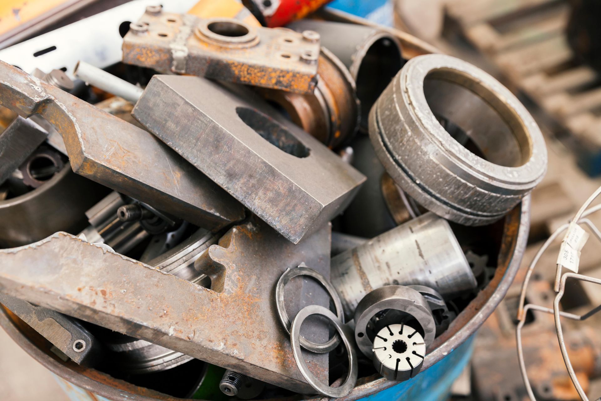 Metal scrap parts in a blue barrel, including gears, rings, and cylinders.
