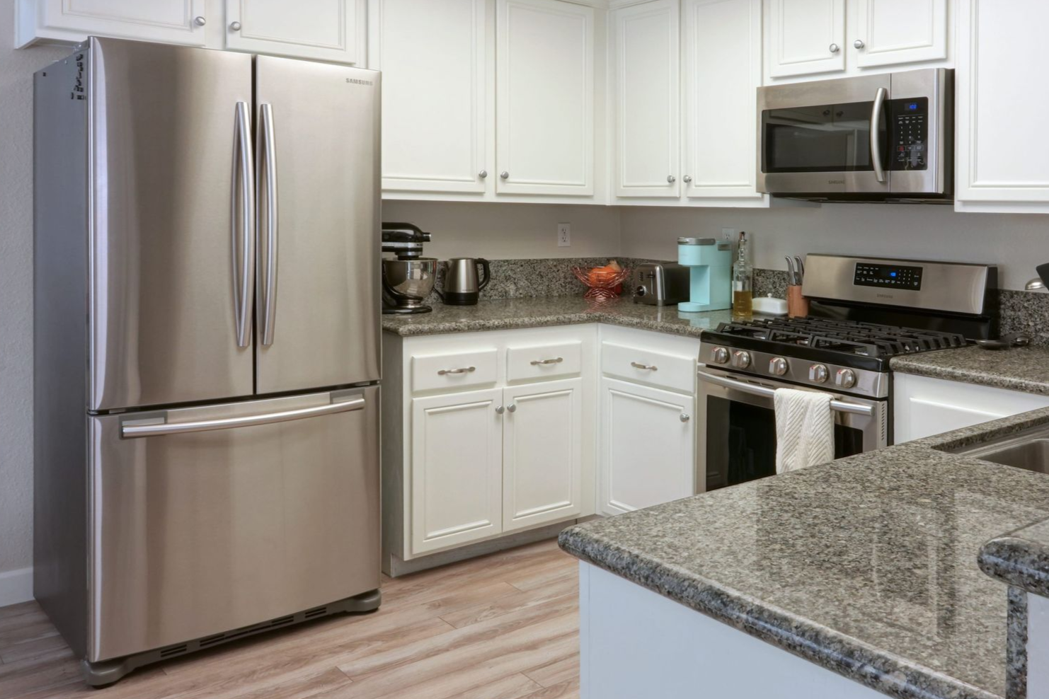Stainless steel refrigerator and appliances in a white kitchen with granite countertops.