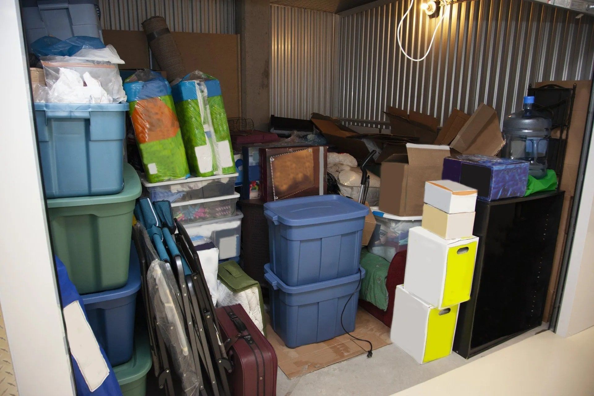 Storage unit filled with stacked blue, green, and white bins, boxes, and miscellaneous items.