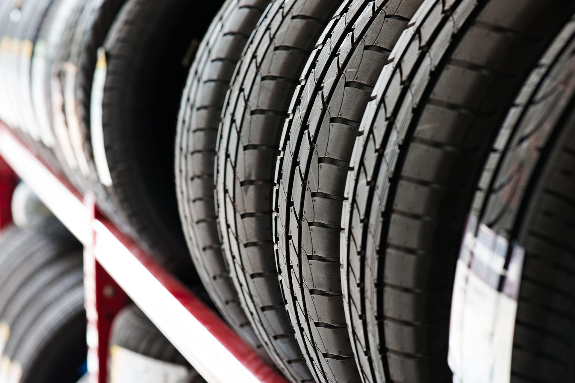 Row of black tires stacked on a red metal rack, ready for sale.