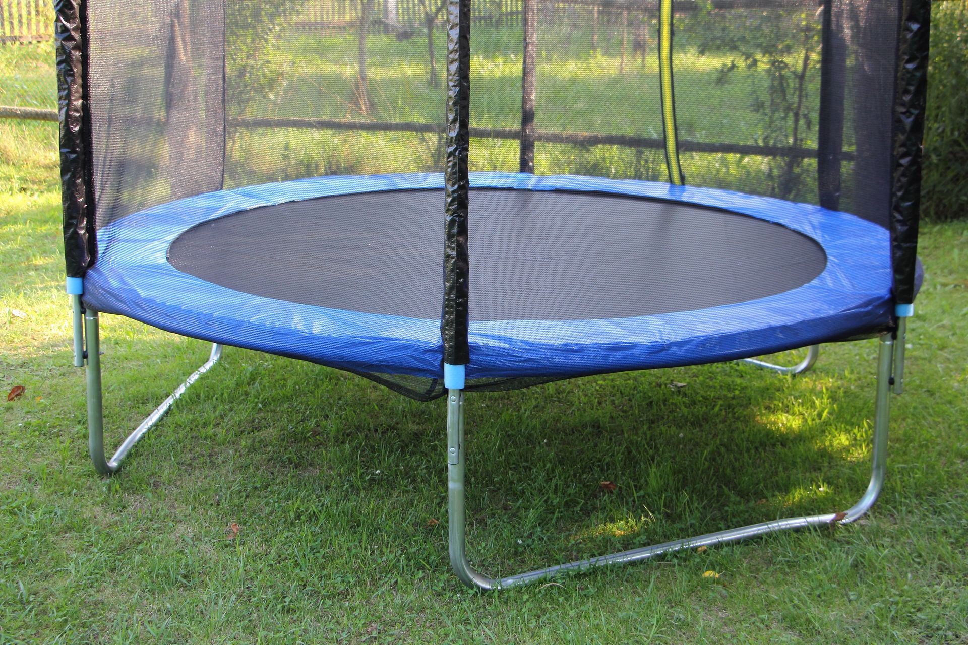 Blue and black trampoline with safety net on green grass.