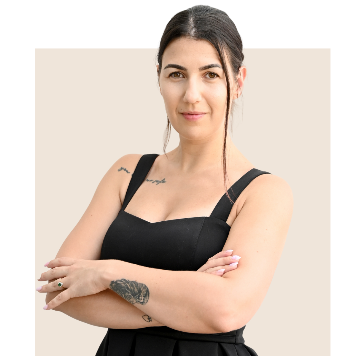 Woman with arms crossed, wearing a black dress, looking at the camera.