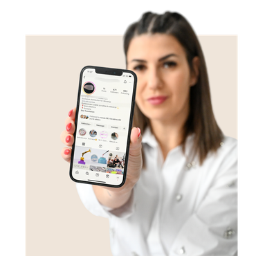 Woman holding a phone displaying a social media profile. She is wearing a white shirt and looking at the camera.