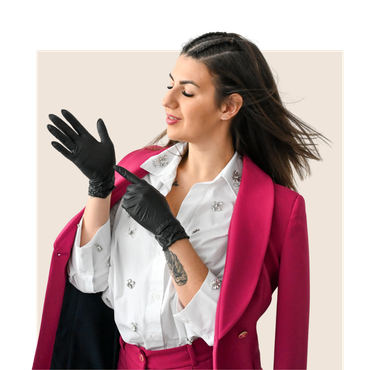 Woman in pink blazer, black gloves, pointing, smiling, wearing white shirt with embellished details.
