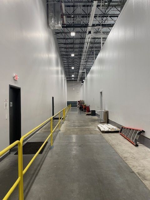 Long hallway with white walls, concrete floor, yellow railing, and overhead lighting.