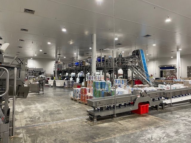Industrial food packaging facility interior with machinery, conveyors, and product.