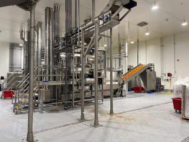 Industrial food processing equipment in a brightly lit factory. Conveyor belt moves product.