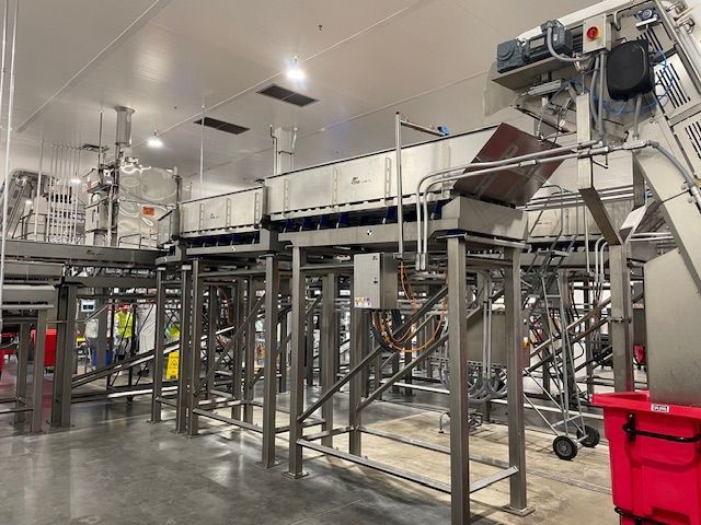 Stainless steel food processing equipment in a brightly lit industrial facility.