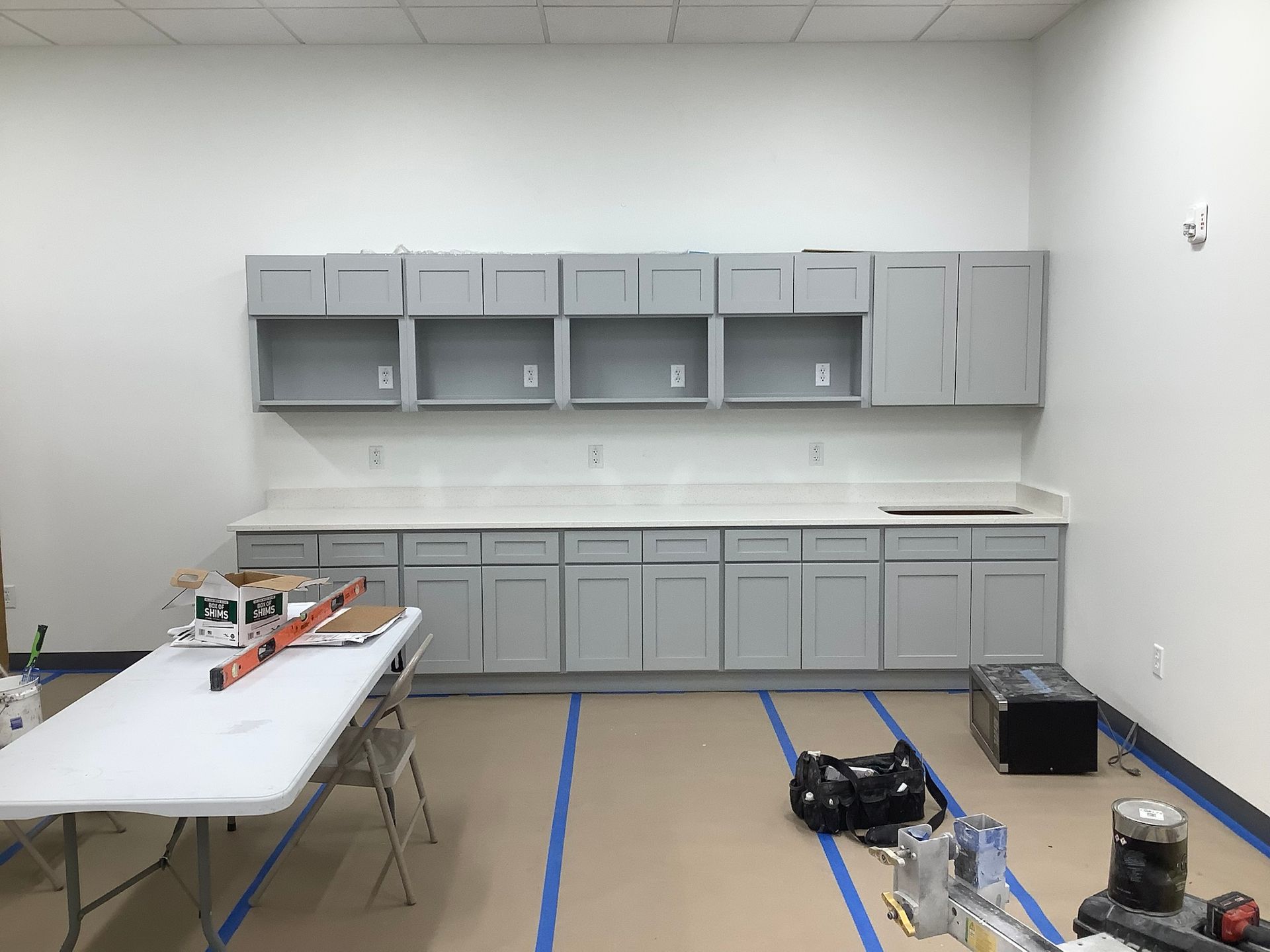 Gray cabinets installed in a room with white walls, countertops, and a folding table.