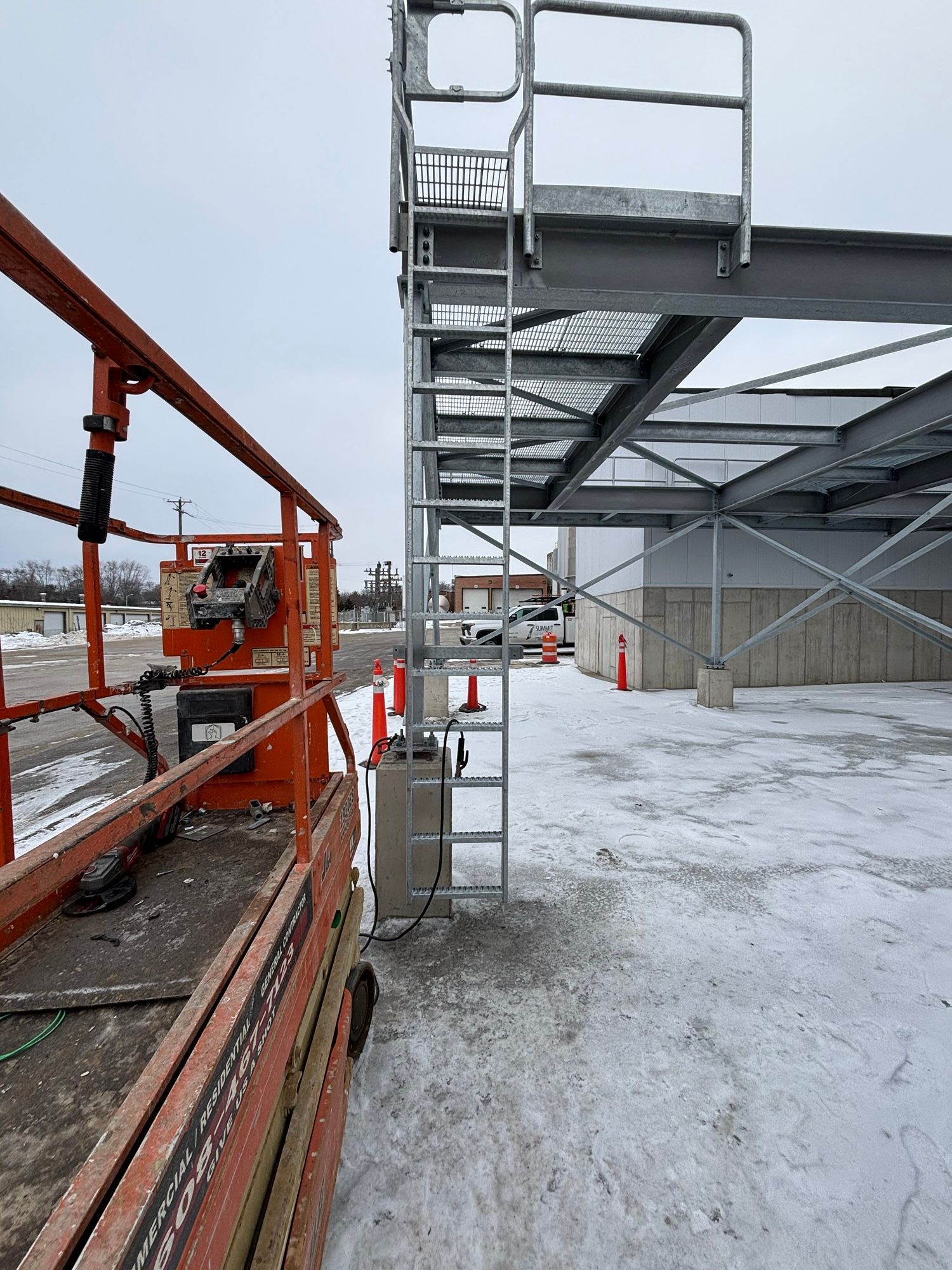 Orange lift next to a ladder leading to a metal platform on a building, construction site.