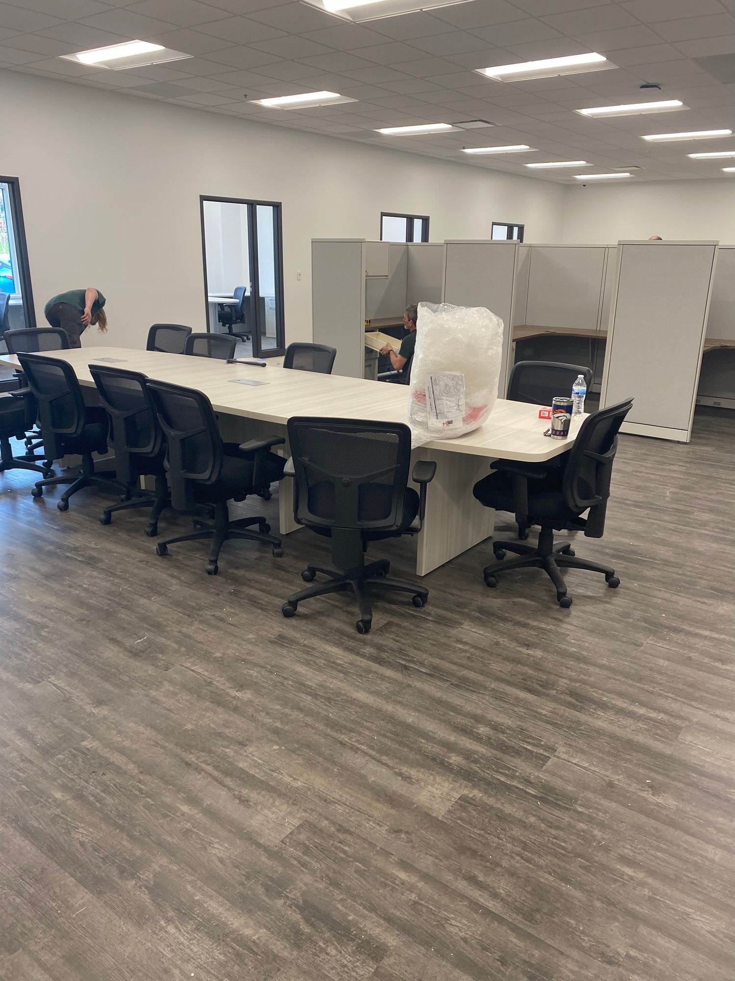 Large conference table with black chairs in an office setting. A person is bending over the table.